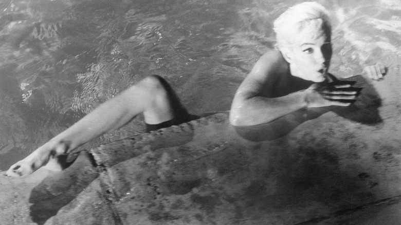 A black and white photo of Marilyn Monroe skinny-dipping, her leg over the side of the pool