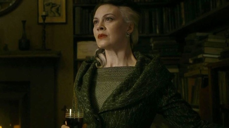 Narcissa Malfoy holds a wine glass with bookshelves behind her