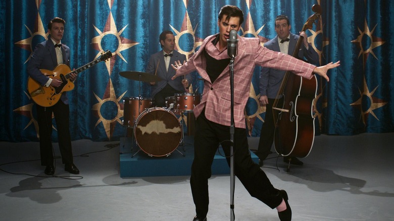 Austin Butler as Elvis Presley singing into a mic in front of Xavier Samuel as Scotty Moore, Terepai Richmond as DJ Fontana, and Adam Dunn as Bill Black on the Milton Berle Show in Elvis.