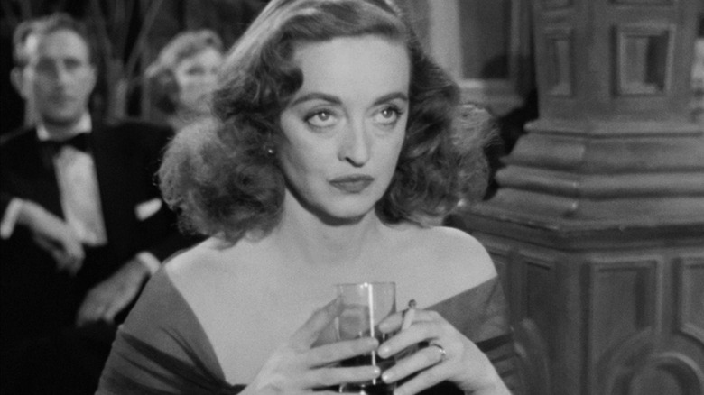 Bette Davis as Margo Channing holding a drink in her hands in All About Eve