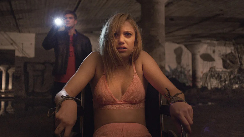 Jay is tied to a chair in her underwear as a man shines a light on something in It Follows