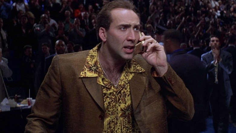 Rick Santoro wearing a brown and bright yellow suit while holding a cell phone in Snake Eyes