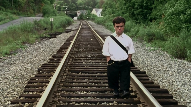 Finbar, with a furrowed brow, walks down the empty train tracks with his hands in his pockets in The Station Agent