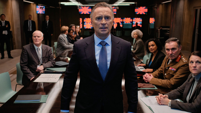 Robert Carlyle as Robert Sutherland, standing in a conference room on Cobra