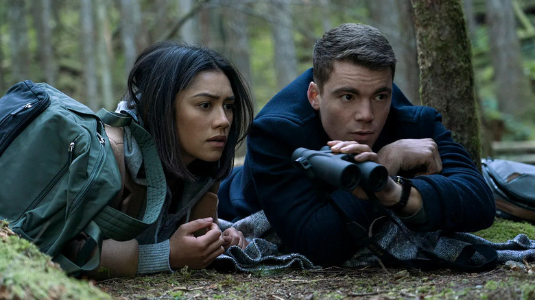 Gabriel Basso and Luciane Buchanan as Peter and Rose, lying on their stomachs in the forest scouting out something.