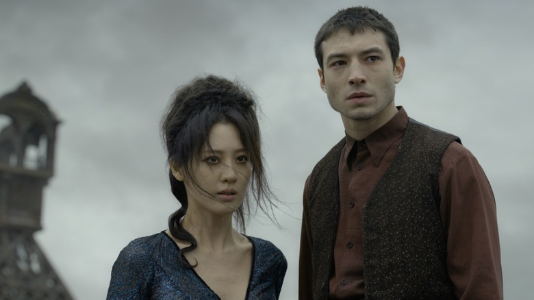 Credence (Ezra Miller) and Nagini (Claudia Kim) stand under a gray sky in Fantastic Beasts: Crimes of Grindlewald