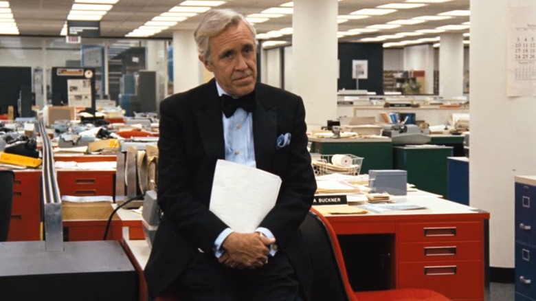 Ben Bradlee sits on a desk at the Washington Post, clutching papers, in All The Presidents Men