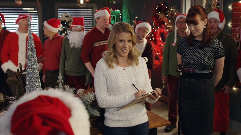 Grace Long writing on a clipboard while men in Santa hats line up behind her, in Finding Santa