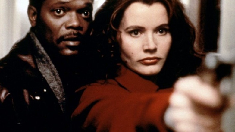 Geena Davis holding a gun with Samuel L. Jackson behind her in A Long Kiss Goodnight