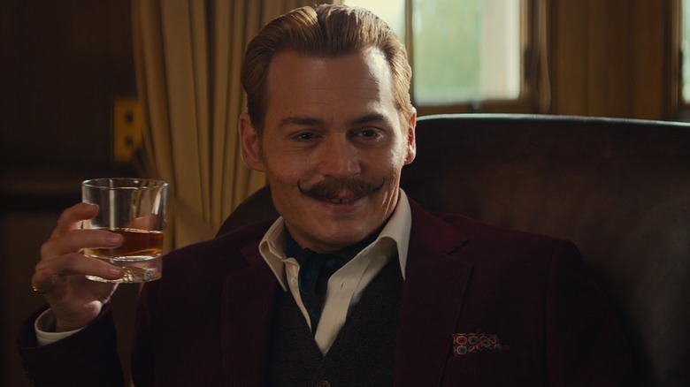 Johnny Depp's Charlie Mortdecai holding up a glass of whisky and smiling in Mortdecai