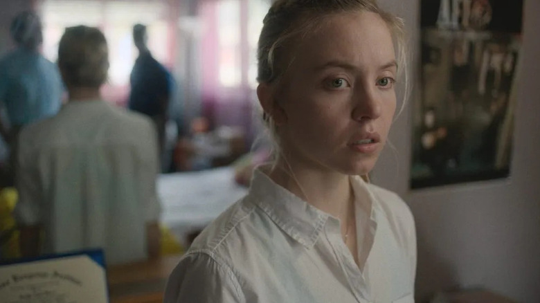 Sydney Sweeney as Reality Winner looking pensive in front of two men with a mirror behind her in Reality