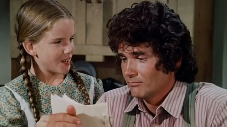 Charles Ingalls (Michael Landon) reads a paper from Laura (Melissa Gilbert) on Little House on the Prairie