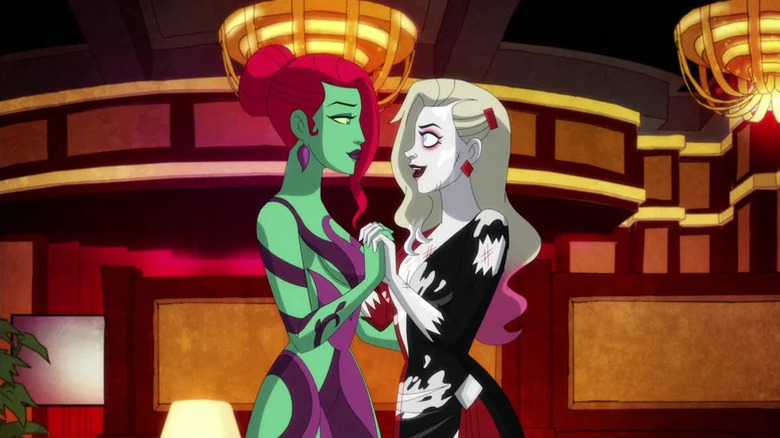 Poison Ivy and Harley Quinn clutching hands while wearing torn dresses in Harley Quinn