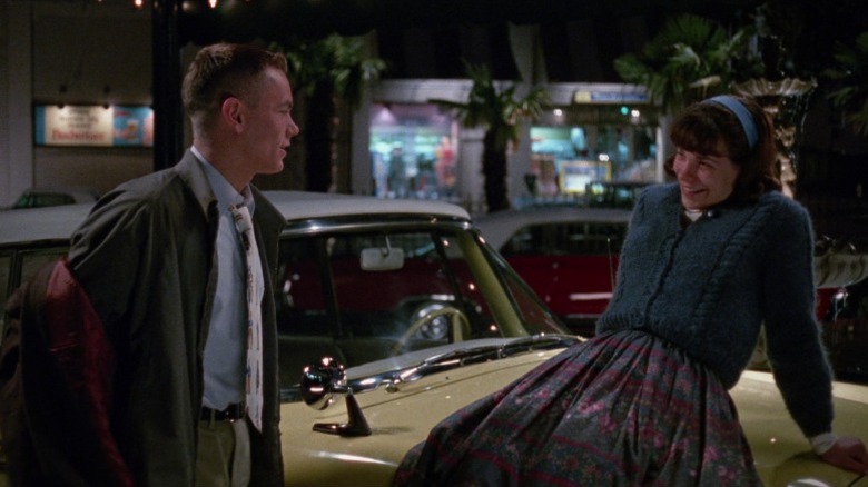 Lili Taylor as Rose Fenny smiling and leaning against a car while looking at River Phoenix as Eddie Birdlace in Dogfight