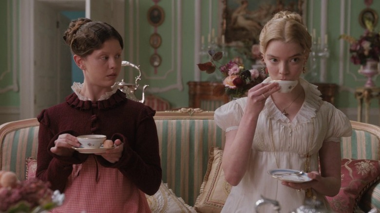 Mia Goth as Harriet Smith and Anya Taylor-Joy as Emma Woodhouse sitting in a couch and drinking tea in Emma.