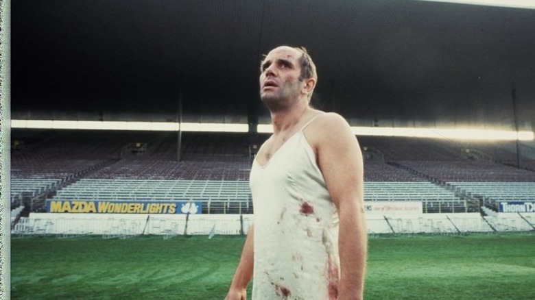 Man in bloodied nightgown standing in empty sports stadium in The Quiet Earth