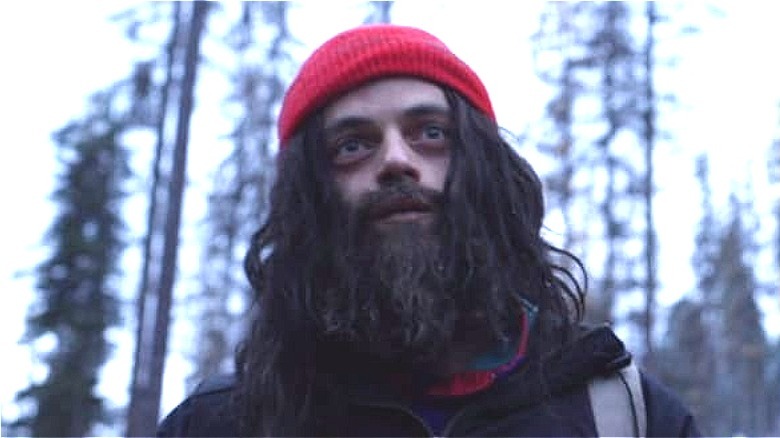 Heavily bearded Rami Malek standing in woods in Buster's Mal Heart