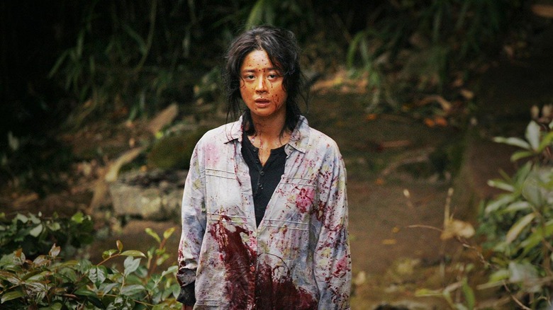 A woman covered in blood stands in the center of the frame.