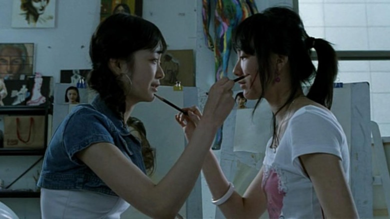 Two women stroke each other's faces with paintbrushes.