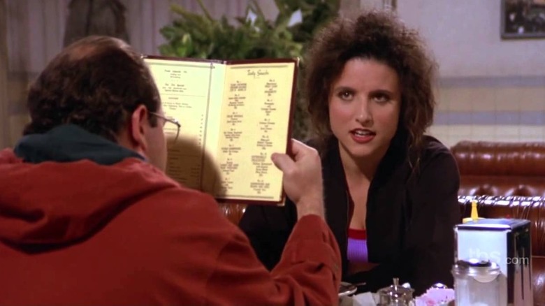 Jason Alexander as George blocking Julia Louis-Dreyfus as Elaine's face with a menu in Seinfeld