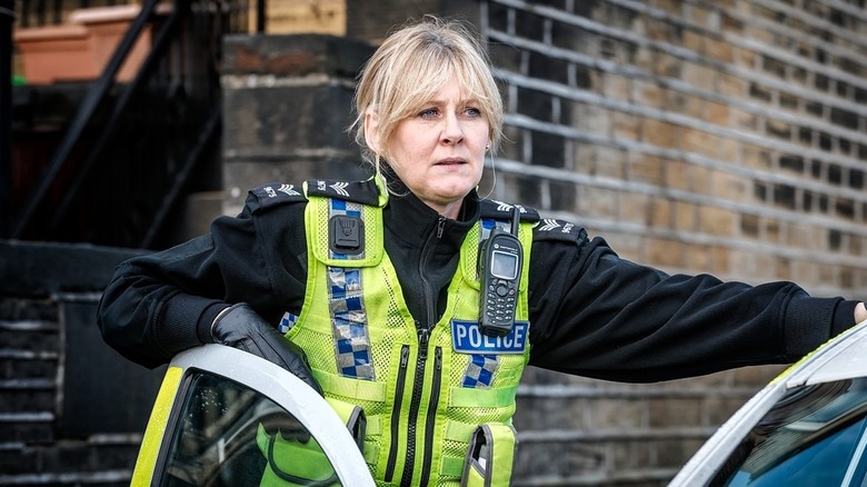 Sarah Lancashire as Catherine Cawood, dressed in uniform and standing next to her car in Happy Valley