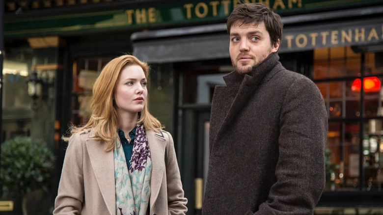 Holliday Grainger and Tom Burke as Robin Ellacott and Comoran Strike standing outside of a pub in Strike