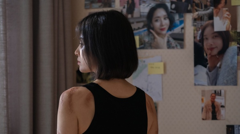 A scarred Moon Dong-eun (Song Hye-kyo) stands before a wall of photos in The Glory