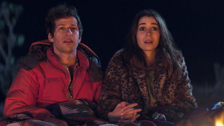 Andy Samberg and Cristin Milioti as Nyles and Sarah holding hands by a fire in Palm Springs