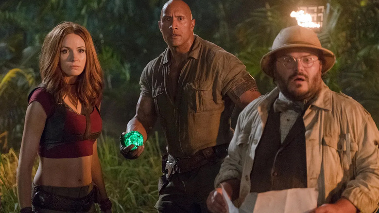 Jack Black as Bethany in her Professor Sheldon Oberon avatar looks at a map in the jungle while standing next to Karen Gillan as Martha in her Ruby Roundhouse avatar with Dwayne Johnson as Spencer in his Dr. Xander Bravestone avatar in Jumanji: Welcome to the Jungle