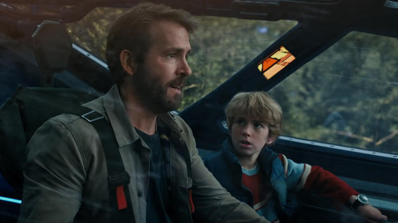 Ryan Reynolds as an older version of Adam Reed sitting with Walker Scobell as a younger version of Adam Reed in a ship cockpit in The Adam Project