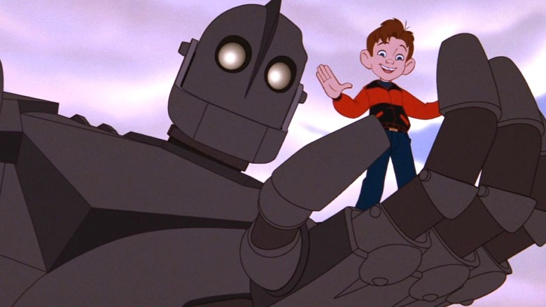 The Iron Giant stands and holds Hogarth in his hand as the both look down in The Iron Giant