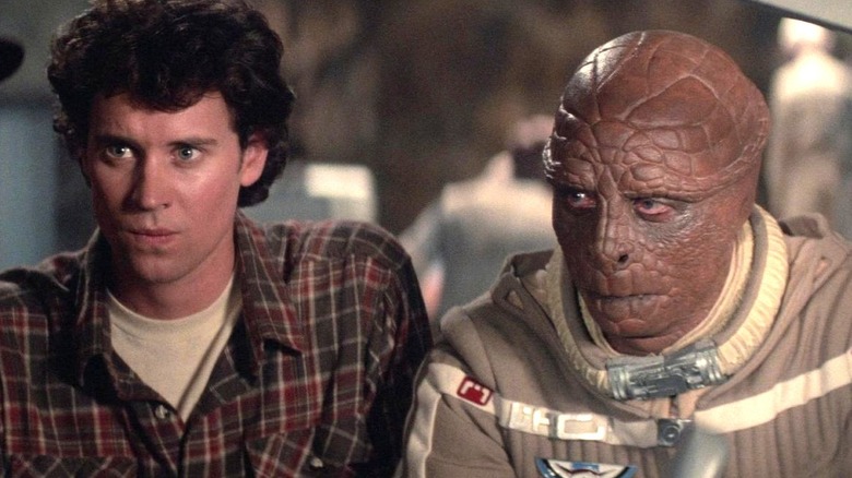 Lance Guest as Alex Rogan wears a plaid shirt while standing next to Dan O'Herlihy as Grig who is wearing a space suit while both of them look toward the left in The Last Starfighter