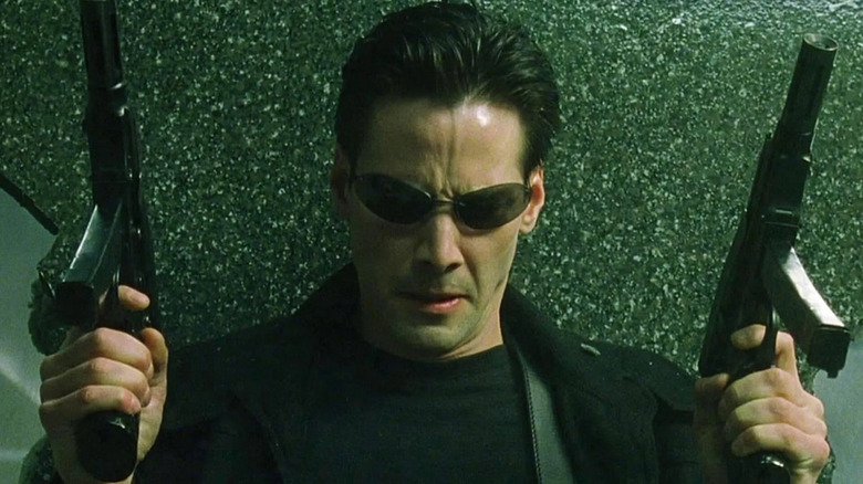 Keanu Reeves as Neo holds two guns in The Matrix