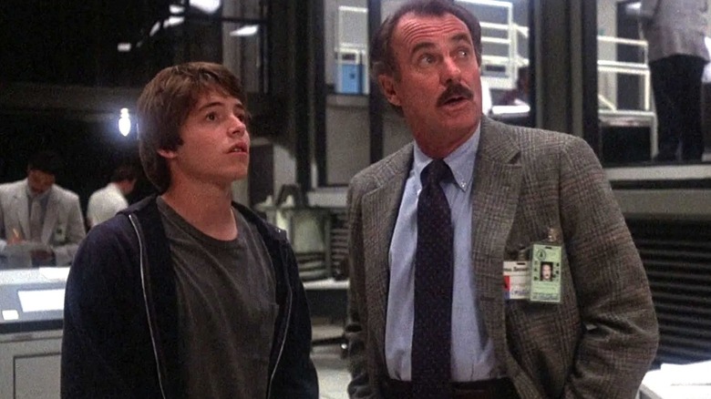 Matthew Broderick as David Lightman stands next to Dabney Coleman as McKittrick as they look up and toward the right while in a military control room