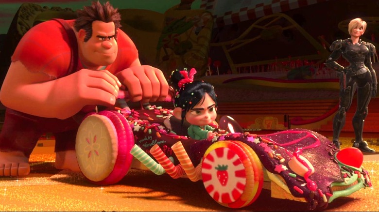 Ralph holds onto the back of Vanellope's race car while she is in the driver's seat and Calhoun stands in the background of the racetrack in Wreck-It Ralph