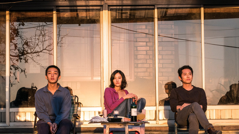 Yoo Ah-in, Jeon Jong-seo, and Steven Yeun as Lee Jong-su, Shin Hae-mi, and Ben, sitting on a porch in Burning