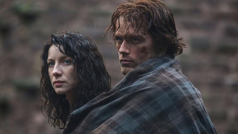 Jamie (Sam Heughan) covers Claire (Catriona Balfe) with a blanket in the rain on Outlander