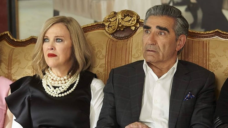 Moira (Catherine O'Hara) sits next to Johnny (Eugene Levy) on a couch in Schitt's Creek