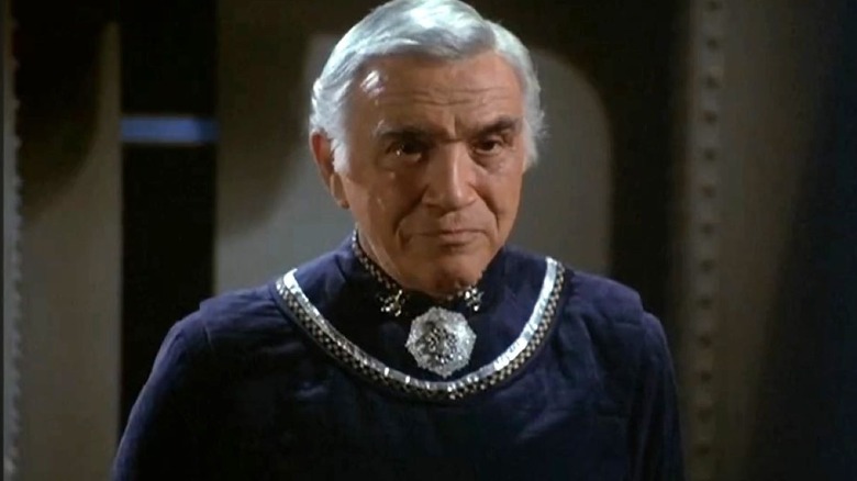 Lorne Greene as Commander Adama stands in blue robes with a silver neckline as he looks ahead on Battlestar Galactica