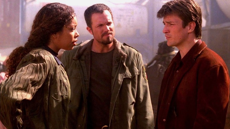 Gina Torres as Zoë Washburne and Nathan Fillion as Captain Malcolm Reynolds stand across from each other with Adam Baldwin as Jayne Cobb behind them on Firefly