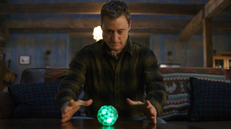 Alan Tudyk as Harry Vanderspeigle sits on a couch as his hands hover over a green orb on Resident Alien