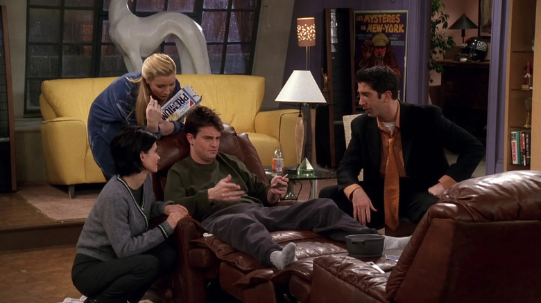 Chandler (Matthew Perry) sits in an armchair comforted by his friends in Friends