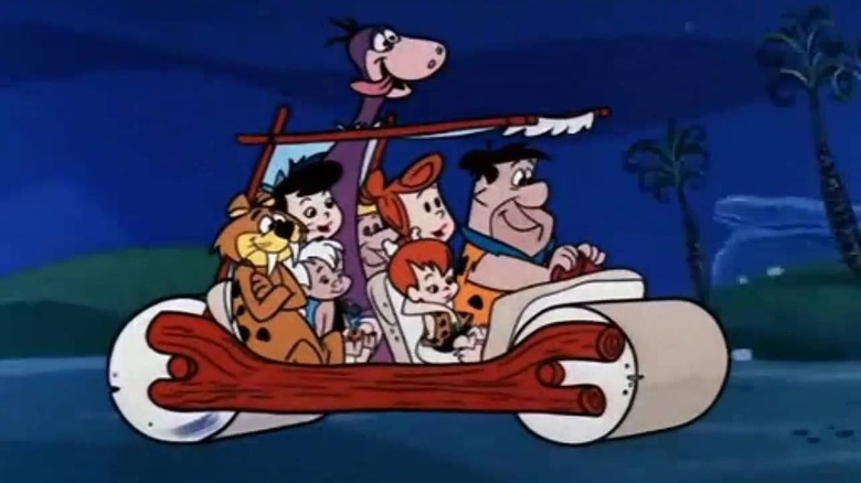 Fred Flintstone (Alan Reed) drives a car full of his family and friends on The Flintstones