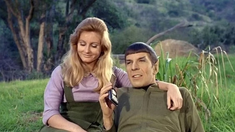 Spock (Leonard Nimoy) happily answers his communicator next to Leila (Jill Ireland) in Star Trek: The Original Series