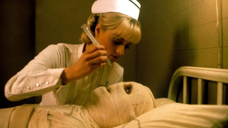 A nurse leans over a bandaged man to stick a needle in his eye