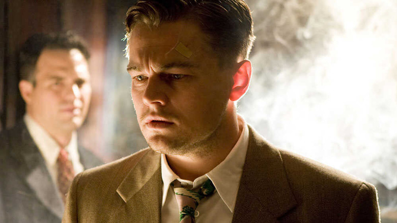 Teddy Daniels (Leonardo DiCaprio) stands in a smoky room watched by Chuck Aule (Mark Ruffalo) in Shutter Island