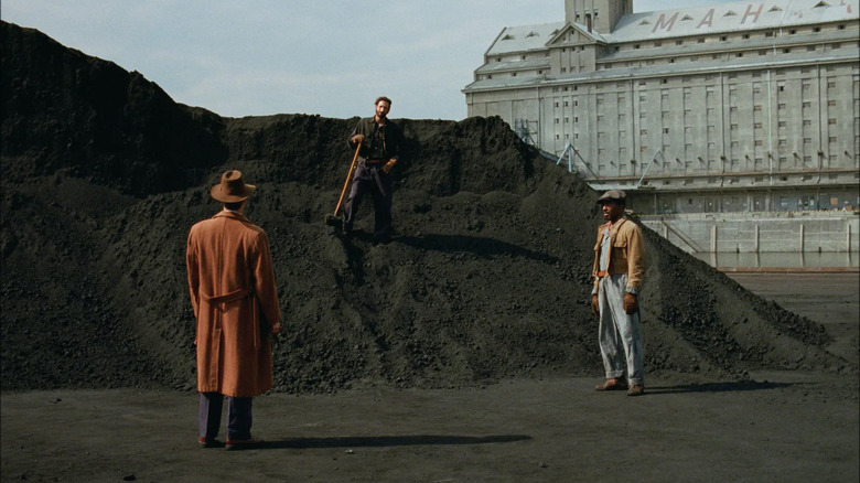 Adrien Brody as Laszlo Toth, shoveling rocks while talking to Guy Pearce in The Brutlalist