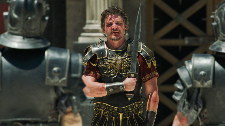 Pedro Pascal's General Acacius bloody and crossing his sword over his chest in Gladiator II