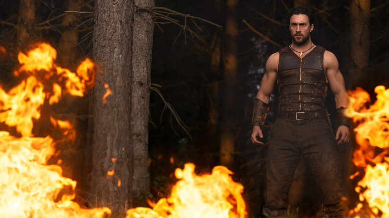 Aaron Taylor-Johnson as Kraven standing amongst flaming trees in the woods in Kraven the Hunter