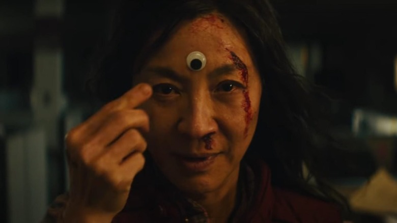 a bloodied woman pointing to a googly eye on her forehead